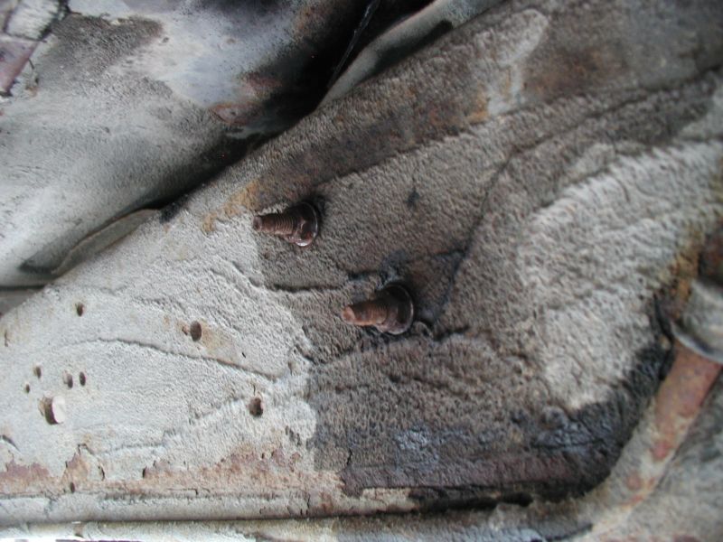 Close-up of two rusty bolts on the underside of a vehicle frame.
