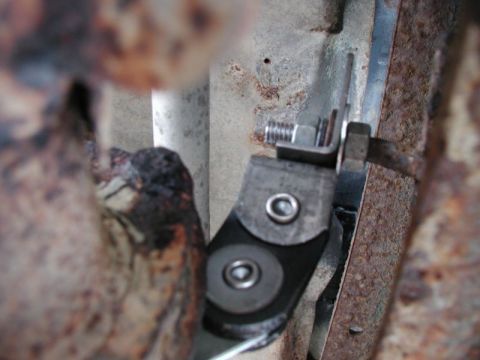 1990 Ford F-250 - A close-up view shows a metal bracket with two rivets attached to a black rubber piece, secured by a bolt and nut to a rusty metal frame. A…
