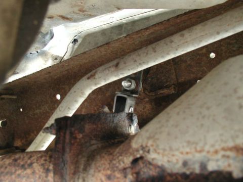 1990 Ford F-250 - A close-up view of the underside of a vehicle, showing rusty metal framing and a section of exhaust pipe. A black bracket with a bolt and n…