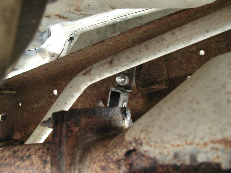 Underside of a vehicle showing rusty frame and exhaust pipe with a mounting bracket.