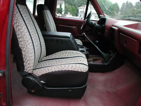 1990 Ford F-250 - The interior of a red Ford F-250 pickup truck shows the driver's side seat with a patterned seat cover and a center console with a gear shi…