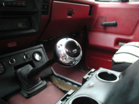 1990 Ford F-250 - The interior of a vehicle shows a chrome aftermarket shift knob on a manual transmission shifter. The dashboard and door panels are a dark…