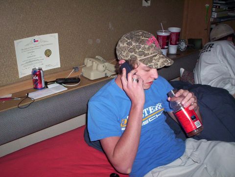 1990 Ford Bronco - A person is seen talking on a cell phone while holding a bottle, with a diploma and soda can visible on a shelf.