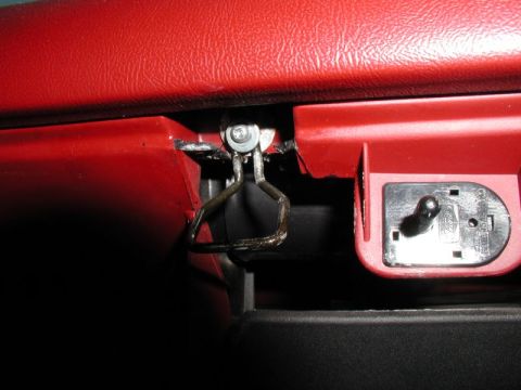 1990 Ford F-250 - A close-up view of a broken red interior car part, possibly a glove box latch mechanism, showing a bent metal wire and a detached plastic p…