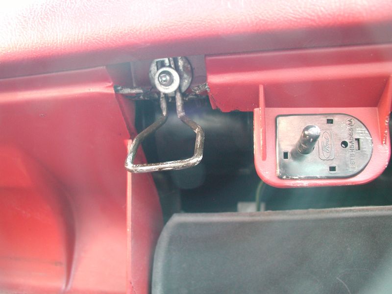 Close-up of broken red glove box latch and Ford latch receiver inside a vehicle.