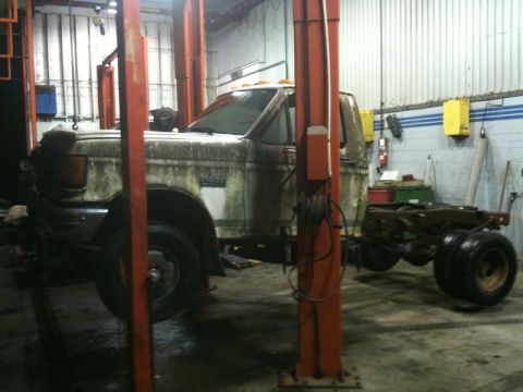 1990 Ford F-250 - A dirty, white pickup truck chassis is raised on a hydraulic lift in a garage. The front of the truck is visible, with the rear section and…