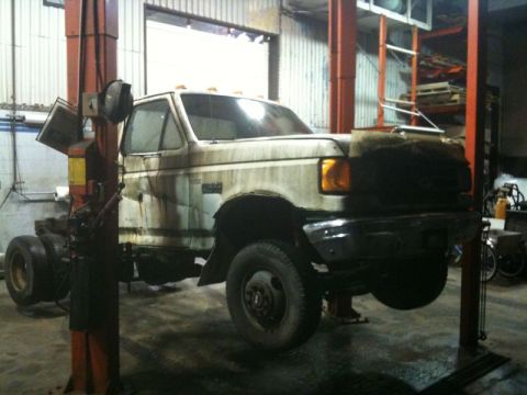 1990 Ford F-250 - A white Ford F-250 pickup truck is raised on a hydraulic lift in a garage. The truck appears to be undergoing maintenance or restoration, w…