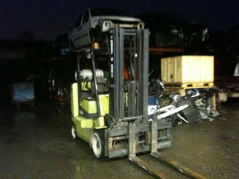 1990 Ford F-250 - A forklift is lifting a car body in a junkyard at night. The forklift is yellow and green, and the car body appears to be silver.