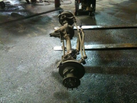 1990 Ford F-250 - A disassembled front axle assembly, likely from a 1990 Ford F-250, is resting on metal supports in a workshop setting. The assembly include…