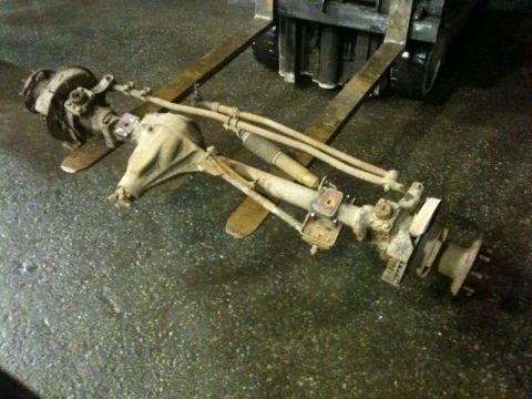 1990 Ford F-250 - A front axle assembly with steering components is shown resting on a forklift. The assembly includes a differential housing, brake componen…