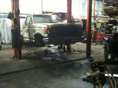 1990 Ford F-250 - A white pickup truck is raised on a hydraulic lift in a garage. The front of the truck is visible, with the hood removed and the grille are…