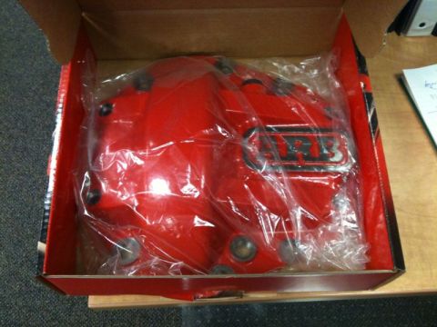 1990 Ford F-250 - A bright red ARB differential cover is shown inside its original cardboard box, still sealed in plastic packaging. The box is open, reveali…
