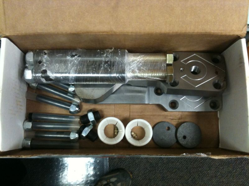 Vehicle suspension or steering parts in a box: bolts, nuts, bushings, and an adjustable component.