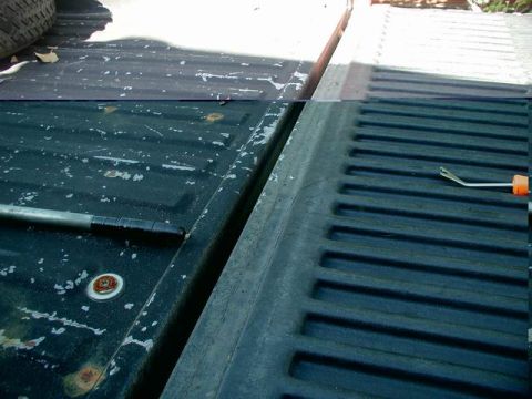 1990 Ford F-250 - The tailgate of a dark-colored pickup truck is shown, with a silver tool with an orange handle resting on the ribbed surface. The truck bed…