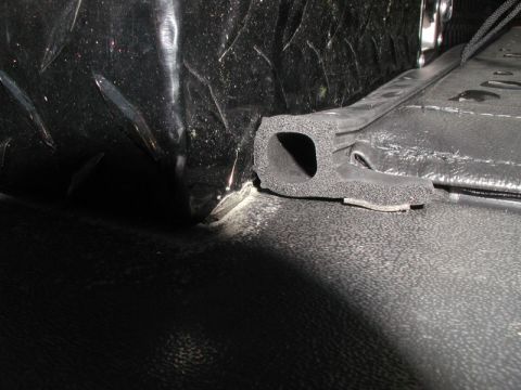 1990 Ford F-250 - A close-up view shows a black rubber seal with a hollow interior, positioned along the edge of a textured black surface. The seal is attach…
