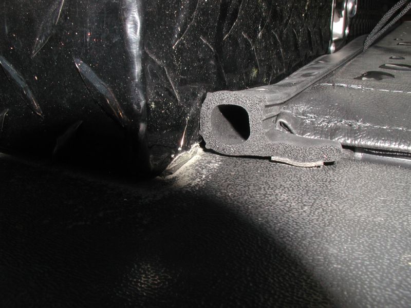 Close-up of a black rubber seal on a textured surface next to diamond-plate metal.