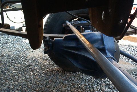 1986 Ford Bronco - Underside view of rear axle and suspension parts, with gravel on the ground.