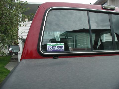 1990 Ford F-250 - The rear passenger side window of a red Ford F-250 pickup truck displays a "BC4X4.COM" sticker. A black tonneau cover is visible over the t…