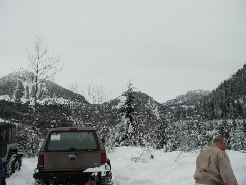 1990 Ford F-250 - The rear of a brown Ford SUV is parked in the snow with snow-covered mountains and trees in the background. A man in a tan jacket stands to…