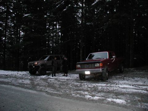 1990 Ford F-250 - A dark, snowy forest scene features two off-road vehicles. A red pickup truck is parked on the right, and a dark SUV is parked on the left…