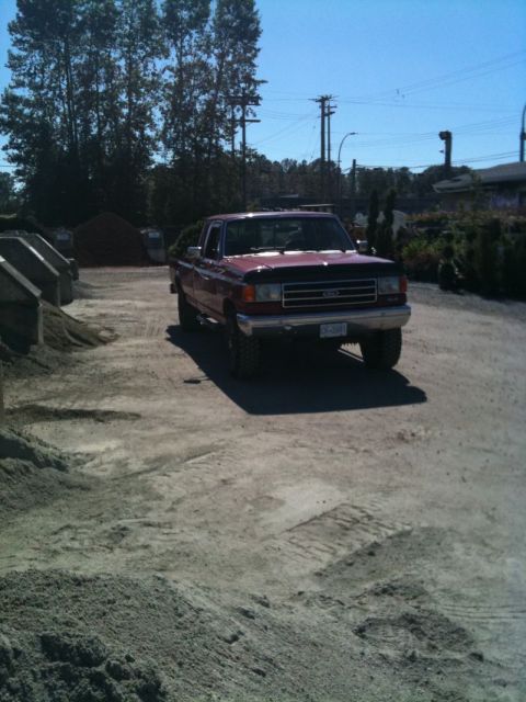 Red 1990 Ford F-250 pickup truck parked in a gravel lot.