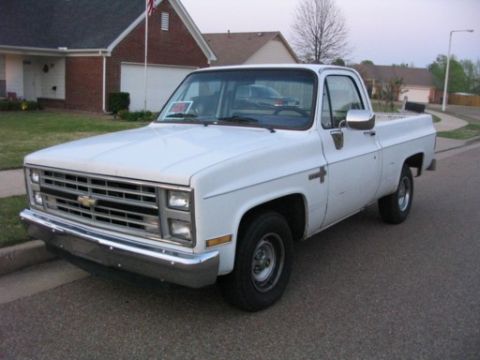 1999 Ford Crown Victoria - This white pickup truck, seen from a 3/4 front angle, appears to be from the 1980s based on its grille design.