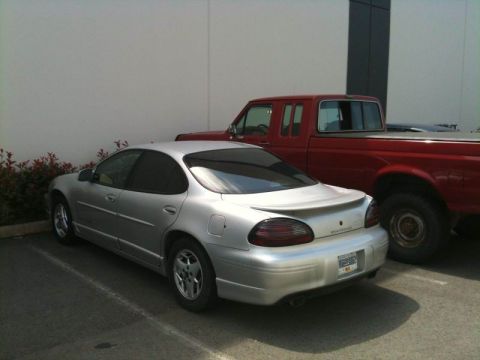 2002 Pontiac Grand Prix - The rear passenger side of a silver 2002 Pontiac Grand Prix is parked next to a red pickup truck. The car has tinted windows and a spoiler.