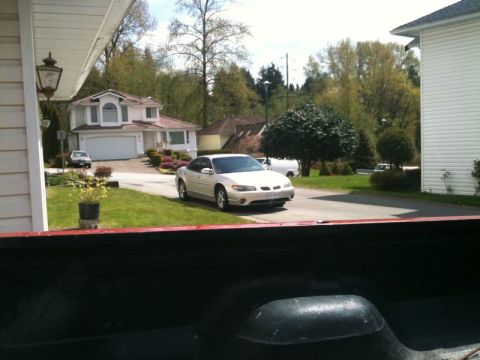 2002 Pontiac Grand Prix - A silver 2002 Pontiac Grand Prix is parked in the driveway of a suburban home. The car is viewed from the perspective of the bed of a picku…