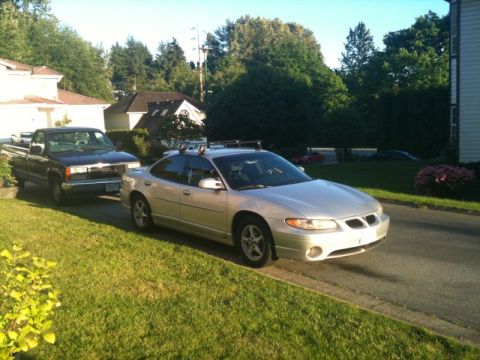 2002 Pontiac Grand Prix - A silver Pontiac Grand Prix sedan is parked on the side of a residential street next to a dark-colored pickup truck. The car has a roof rac…