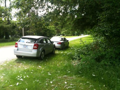 2002 Pontiac Grand Prix - A silver hatchback is parked on the side of a gravel road, with another silver car parked behind it. The scene is bordered by a grassy area…