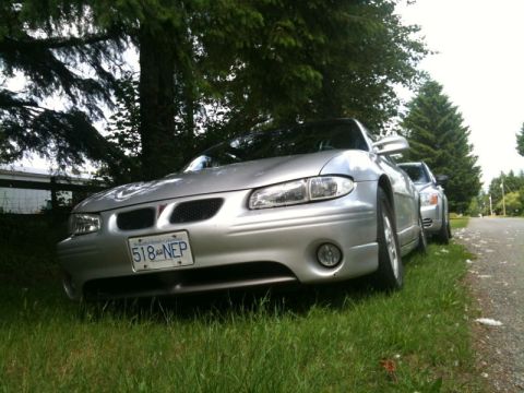 2002 Pontiac Grand Prix - A silver Pontiac Grand Prix is parked on a grassy shoulder next to a gravel road, with another silver car visible behind it. The car is fac…