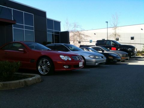 2002 Pontiac Grand Prix - A line of cars is parked in front of a modern building. The closest vehicle is a red coupe, followed by a silver sedan, a black coupe, and…