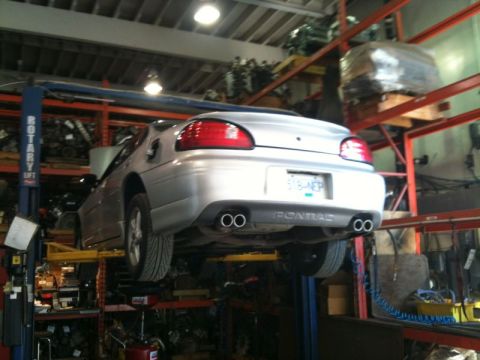 2002 Pontiac Grand Prix - A silver Pontiac Grand Prix is shown from the rear, elevated on a car lift in an auto repair shop. The car has dual exhaust pipes and a lic…
