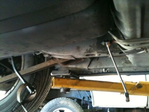 2002 Pontiac Grand Prix - Underneath a vehicle, a wrench is used to tighten a bolt on a fuel line near the fuel tank. The vehicle is supported by a yellow lift.