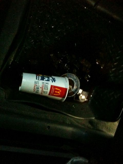 2002 Pontiac Grand Prix - A McDonald's cup is lying on its side on a wet, dark surface, possibly the floor of a car. The cup has the McDonald's logo and text that re…