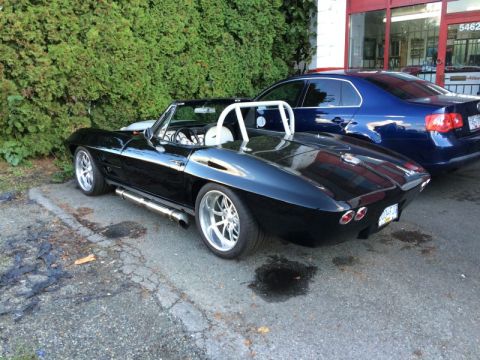 2002 Pontiac Grand Prix - A black convertible sports car with a white roll bar is parked next to a hedge and a blue sedan. The car has custom chrome wheels and side…
