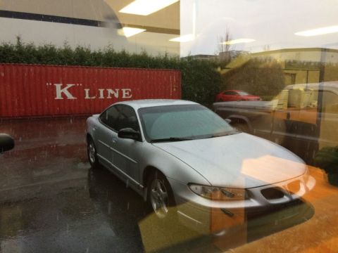 2002 Pontiac Grand Prix - A silver Pontiac Grand Prix is parked on a wet asphalt lot in front of a red shipping container with white text that reads "K LINE". The sc…
