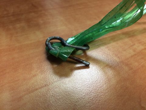 2002 Pontiac Grand Prix - A close-up shot shows a metal loop attached to a piece of green plastic, which is connected to a metal pin. The object rests on a wooden su…