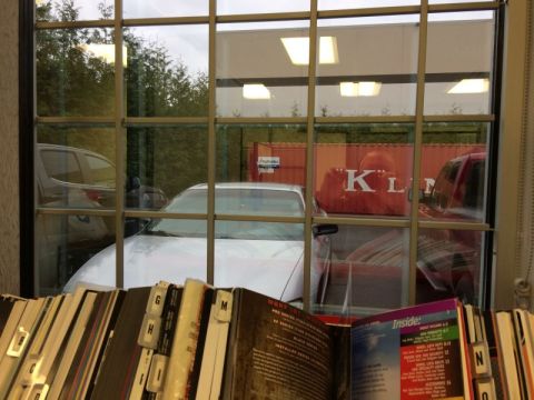2002 Pontiac Grand Prix - A white sedan is parked behind a row of magazines, viewed through a window with a grid of panes. A red shipping container with white letter…