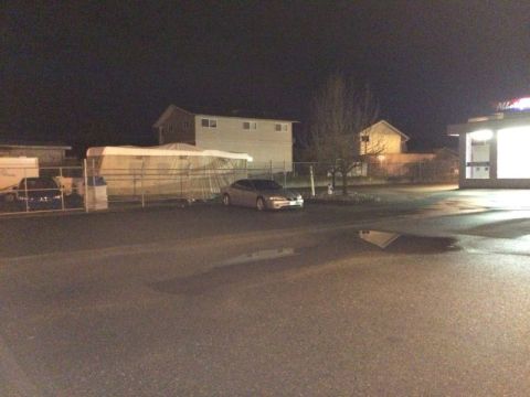2002 Pontiac Grand Prix - A silver sedan is parked in a lot at night, with a large structure covered in a tarp behind a fence to its left. A brightly lit building wi…