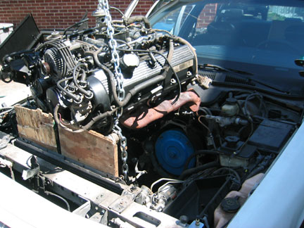 1996 Ford Crown Victoria - The engine is being removed from the vehicle, supported by wooden blocks and chains.