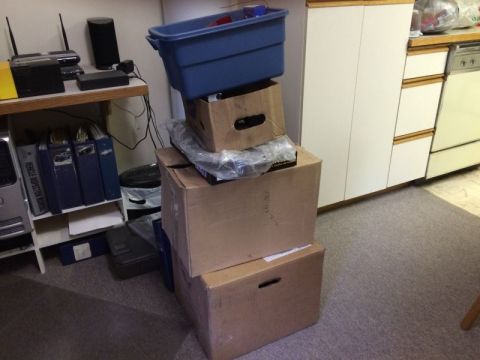 2002 Pontiac Grand Prix - A stack of cardboard boxes and a blue plastic bin are piled on the floor next to a shelf with binders and electronic devices. A kitchen cou…