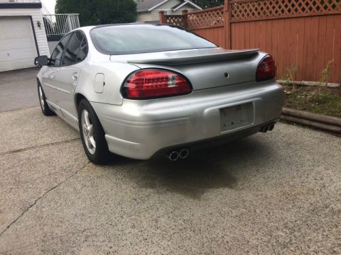 2002 Pontiac Grand Prix - Rear 3/4 view of a silver Pontiac Grand Prix parked on a concrete driveway. The car features a rear spoiler and dual exhaust pipes.