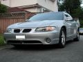 2002 Pontiac Grand Prix - A silver 2002 Pontiac Grand Prix is parked on a residential street. The front 3/4 view shows the car's headlights, grille, and front bumper.