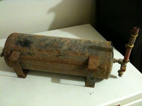2002 Pontiac Grand Prix - A rusty, cylindrical air tank with two mounting brackets is shown resting on a white surface. A brass fitting with a red tube and yellow ba…