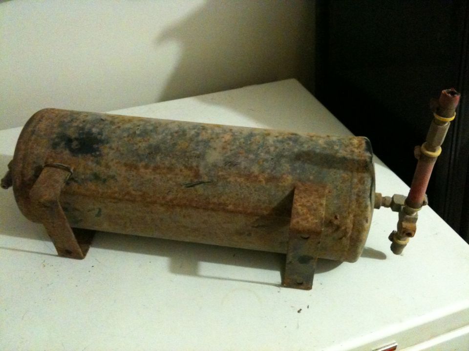 Rusty air tank with mounting brackets and brass fitting with red tube