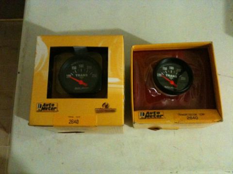 2002 Pontiac Grand Prix - Two Auto Meter transmission temperature gauges are displayed in their original yellow packaging. Both gauges show a reading between 150 and…