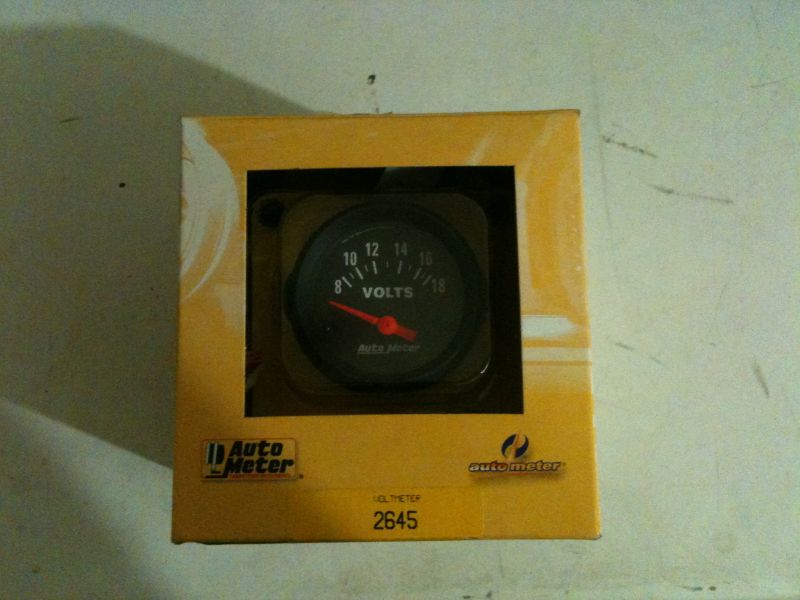 Yellow box with cutout showing an Auto Meter voltmeter gauge.