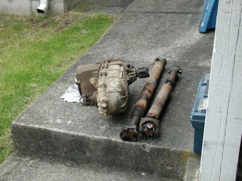 2002 Pontiac Grand Prix - A transfer case and two driveshafts are laid out on concrete steps next to a grassy area. A white downspout is visible on the left.