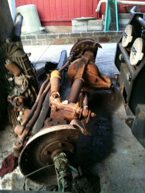 2002 Pontiac Grand Prix - This is a close-up, overhead view of a heavily rusted automotive rear axle assembly with brake components. Two white IPF lights are visible…